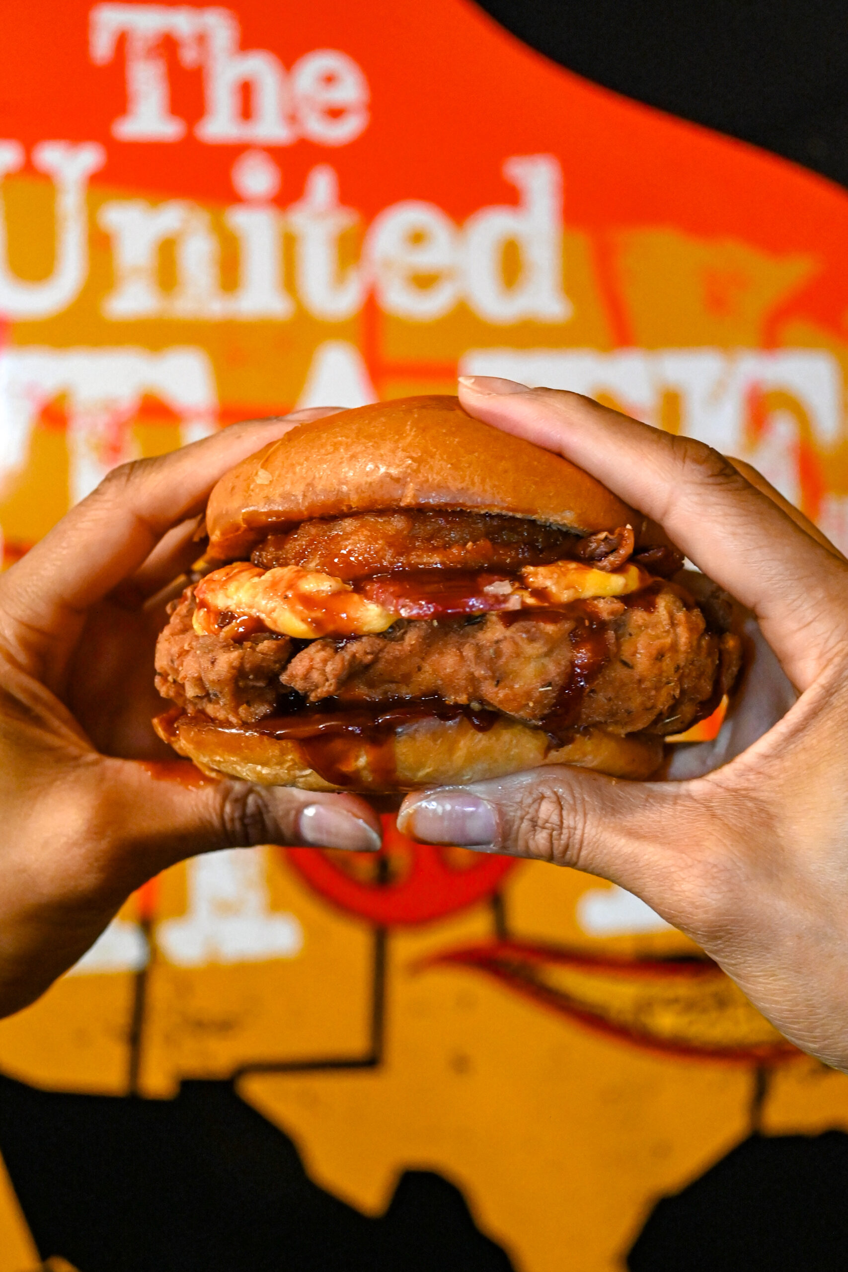 Image of a burger being held by two hands with an orange background